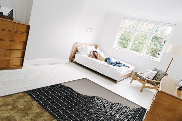 Ein Schlafzimmer mit einem Bett, der halbe Fußboden ist noch offen und zeigt die Bestandteile der Fußbodenheizung.
