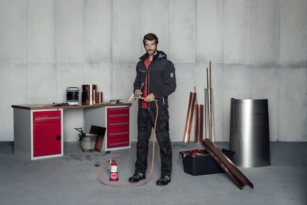 Ein Mann steht in Arbeitskleidung in einer Werkstatt.