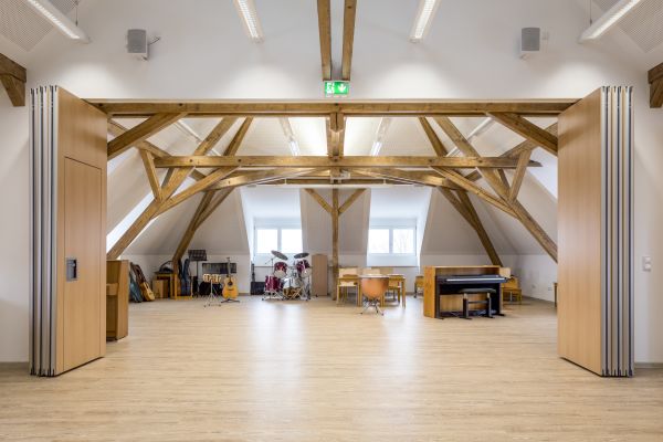 Ein Zimmer voller Musikinstrumente in einem Dachgeschoss mit Holzbalken.