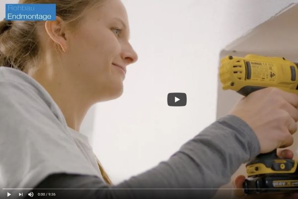Screenshot aus einen Installationsvideo, eine Frau bohrt mit einer Bohrmaschine in die Wand.