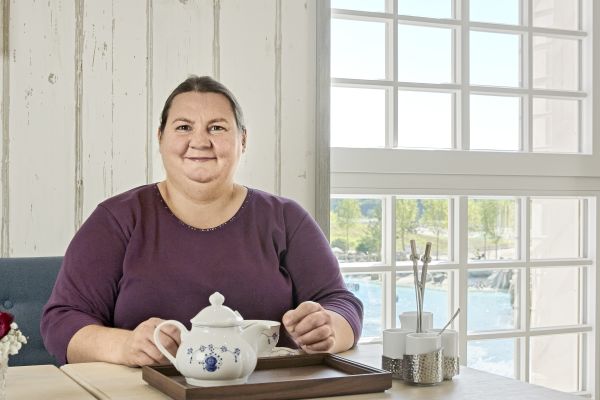 Eine Frau sitzt an einem Tisch, vor ihr steht eine Teekanne auf einem Tablett.
