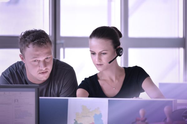 Ein Mann und eine Frau mit Headsets sitzen vor einem Computer.