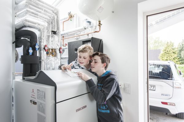 Zwei Kinder stehen an einer Wärmepumpe in einem Heiztechnikraum.