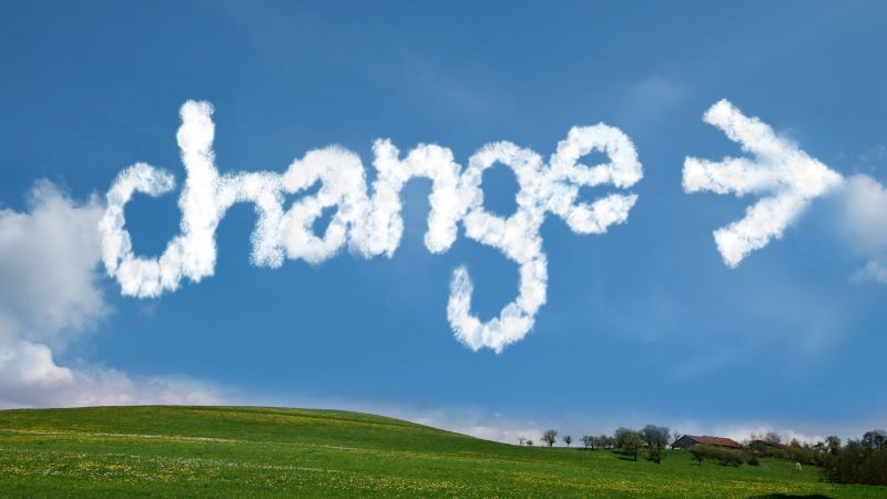 Das Wort Change wie aus Wolken gemalt auf einem Himmel über einer grünen Wiese.