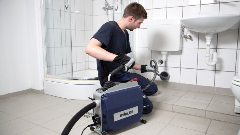 Ein Handwerker reinigt mit einer Rohrreinigungsmaschine ein Rohr in einem Bad.