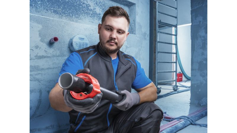 Das Bild zeigt einen Handwerker auf der Baustelle, der den Rohrabschneider um ein Kunststoffrohr hält.