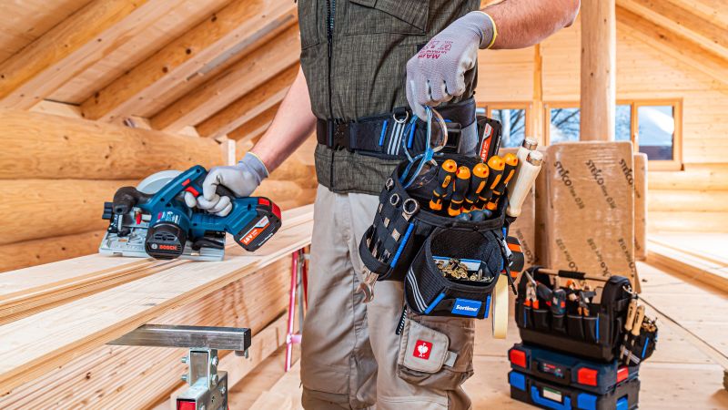 Ein Handwerker mit einem Werkzeuggürtel und einer Werkzeugtasche ausgestattet auf einer Baustelle in einem Holzhaus.