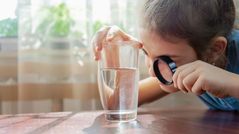 Das Bild zeigt ein Kind mit Lupe und Wasserglas.