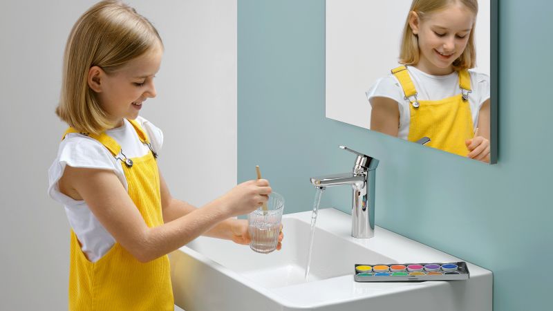 Das Bild zeigt ein Mädchen mit einem Pinselglas am Waschbecken.