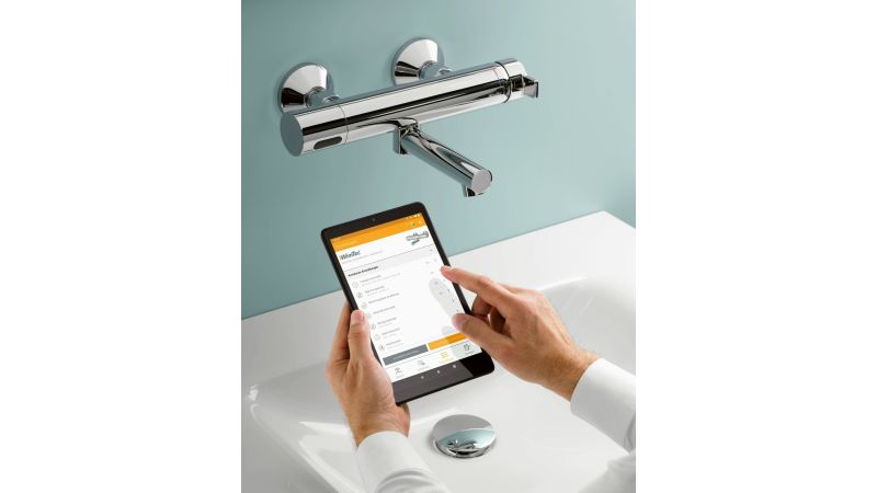 Das Bild zeigt eine Hand, die ein Tablet in einem Waschraum hält.
