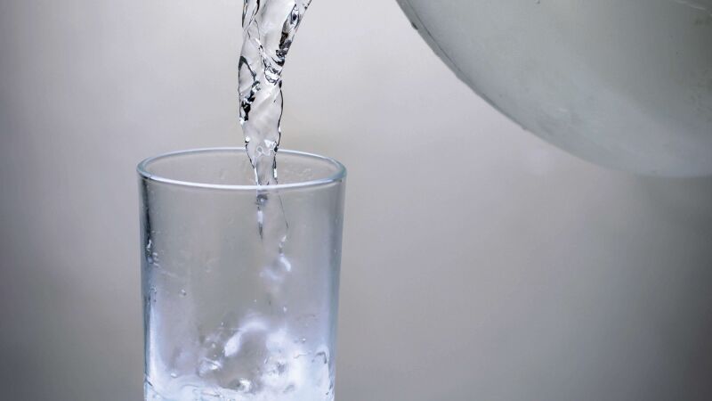 Das Bild zeigt ein Glas, das mit Wasser aus einer Glaskanne gefüllt wird.