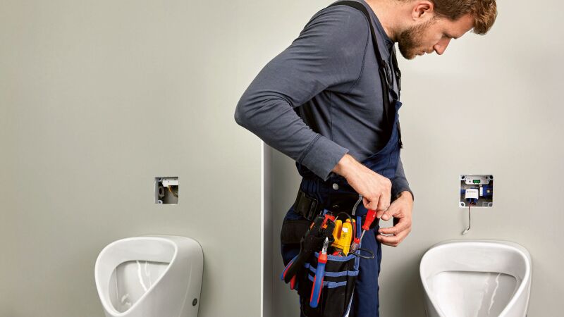 Das Bild zeigt einen Handwerker an einem Urinal.