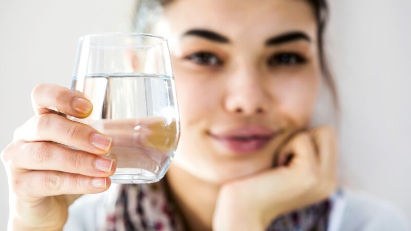 Das Bild zeigt eine Frau, die ein Wasserglas hält.