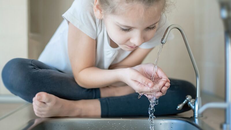 Das Bild zeigt ein Mädchen, das Wasser aus einer Armatur trinkt.