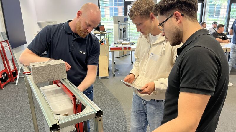 Das Bild zeigt Philipp Hagedorn, TECE Außendienst, der die Auszubildenden bei der Installation einer TECEsolid WC-Betätigungsplatte unterstützt.