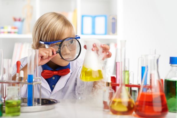 Ein Kind betrachtet mit einer Lupe ein mit gelber Flüssigkeit gefülltes Reagenzglas. 