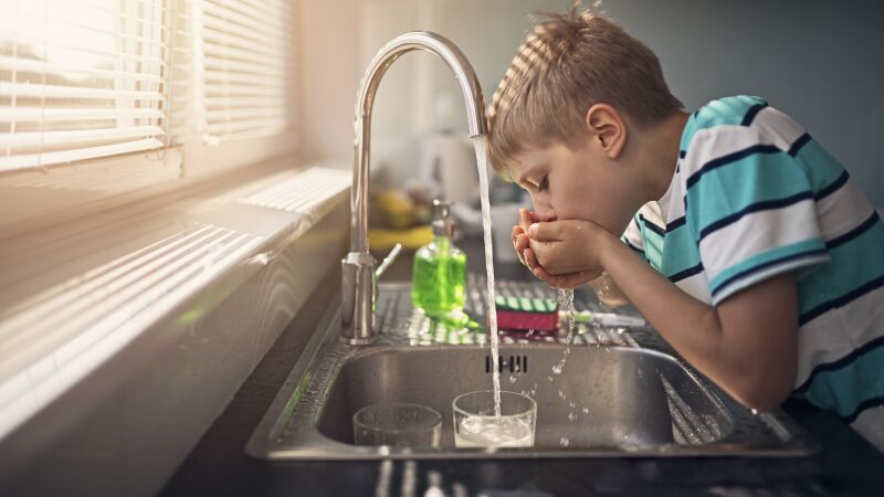 Das Bild zeigt einen Jungen, der Wasser aus einer Armatur trinkt.