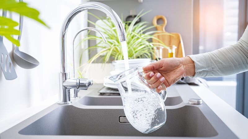 Das Bild zeigt eine Hand mit Wasserkanne, die gefüllt wird.