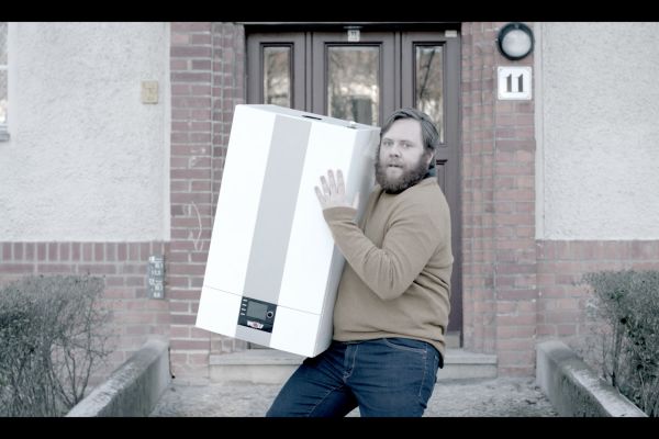 Ein Mann steht mit einer Therme auf dem Arm vor einer Haustür.