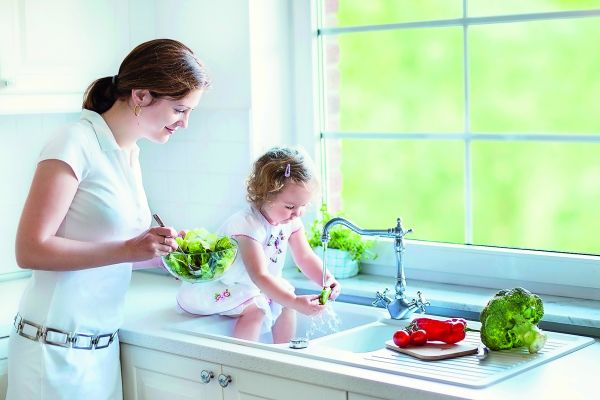 Eine Frau und ein Mädchen waschen an einem Küchen-Wasserhahn Gemüse.