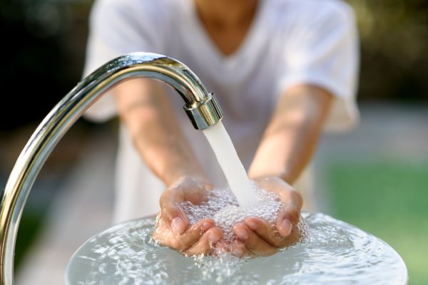Ein Kind wäscht sich unter einem Wasserstrahl aus einem Wasserhahn die Hände.