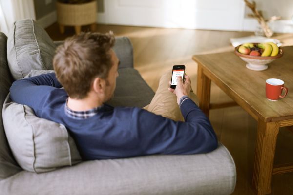 Ein Mann sitzt mit einem Smartphone auf einem Sofa.