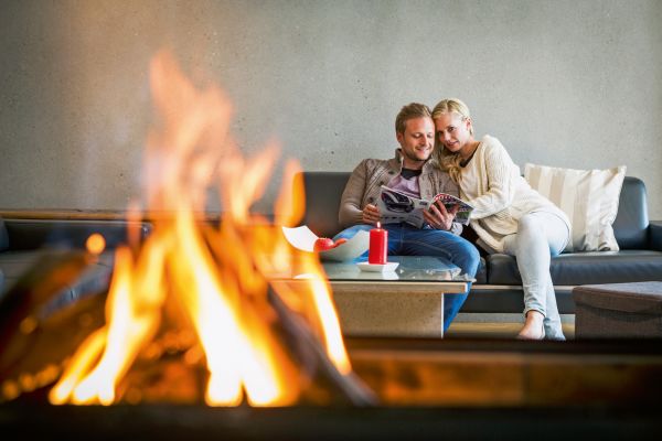Ein Paar sitzt auf einem Sofa, im Vordergrund brennt ein Feuer.