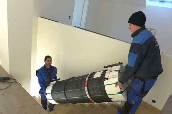 Zwei Handwerker tragen einen Kunststoff-Wärmetank eine Treppe hinauf.