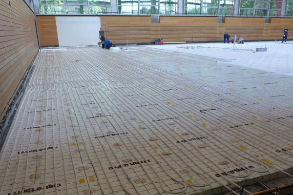 Fußbodenheizungsrohre auf dem Boden einer Sporthalle.