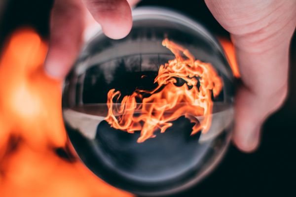 Eine Hand hält eine Glaskugel, in der sich ein Feuer spiegelt.