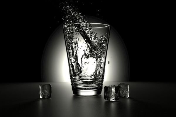 Ein Glas Wasser auf einem Tisch, daneben Eiswürfel.