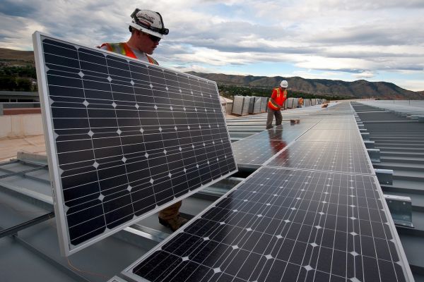 Zwei Handwerker installieren Solarmodule auf einem Dach.