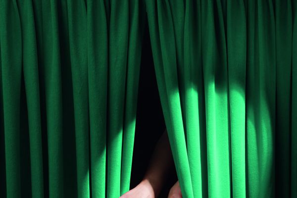 Das Bild zeigt einen von zwei Händen geöffneten, grünen Vorhang.
