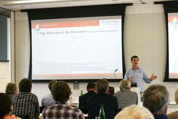 Ein Mann hält vor einer Leinwand mit einer Powerpoint-Präsentation einen Vortrag.